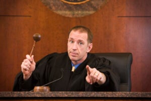 digital accomplice Upset judge pointing with a gavel in hand.